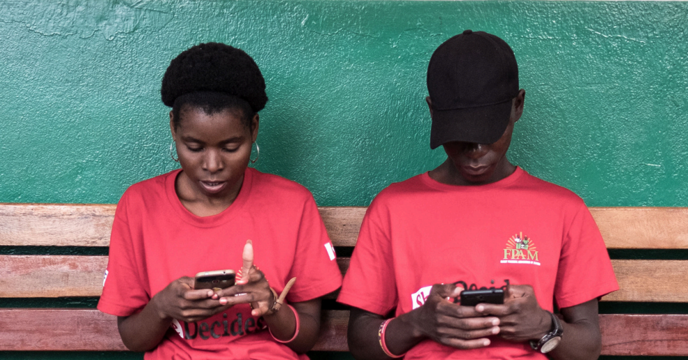 two young people sitting on a bench using their phones