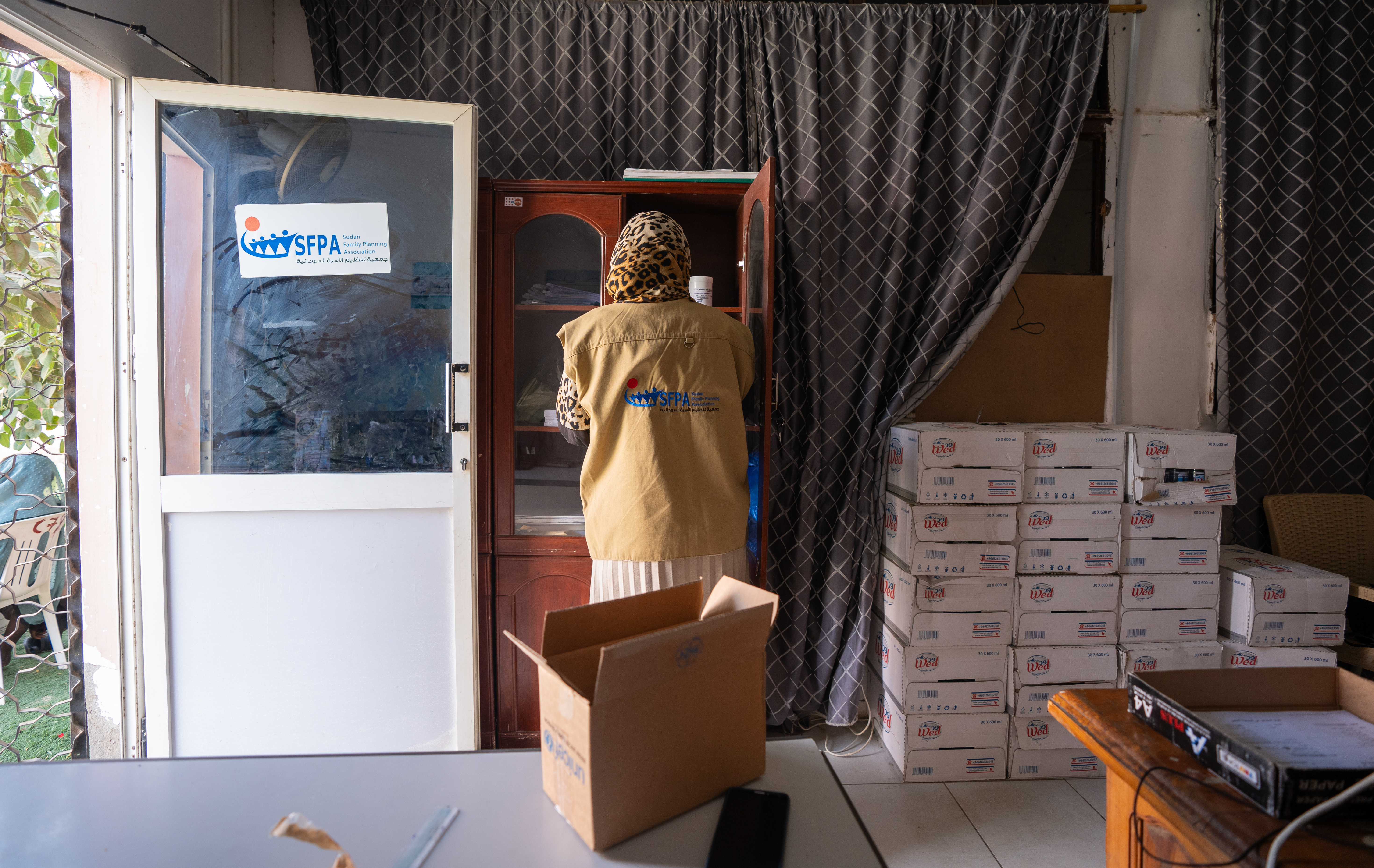 Member of the Sudan Family Planning Association with her back to the camera as she loads materials into a brown cupboard. 
