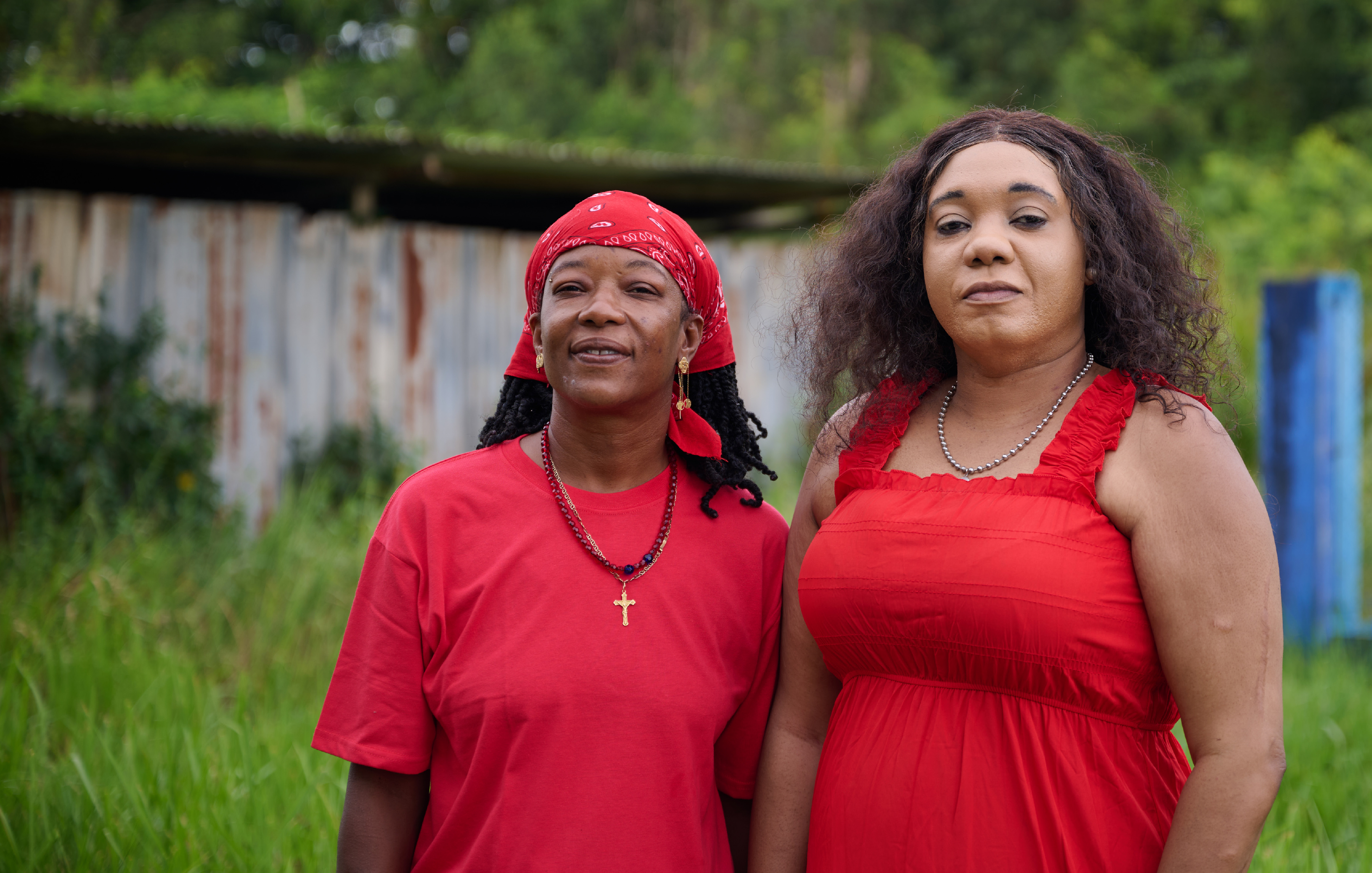 Two community workers in Suriname face the face camera, both dressed in red.