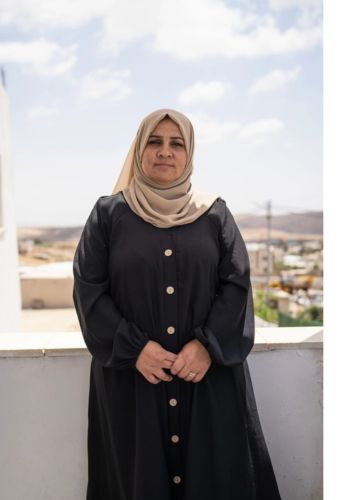 Aida stands on the balcony of the mobile clinic. She wears a black dress and beige headscarf