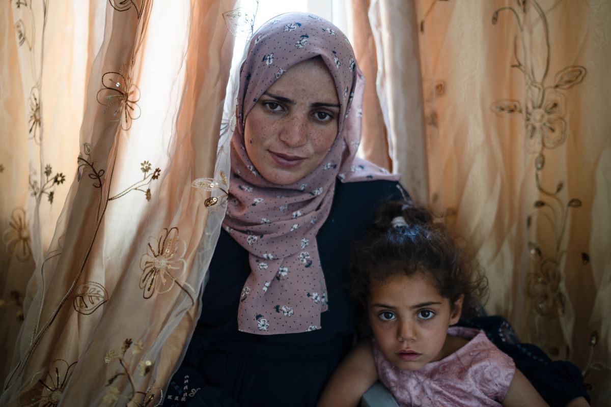 Hiba wearing a pink headscarf sits with her daughter in front of a curtain