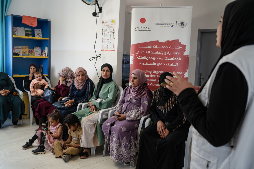 A healthcare professional speaks to a group of women in a waiting room at a mobile clinic in the West Bank