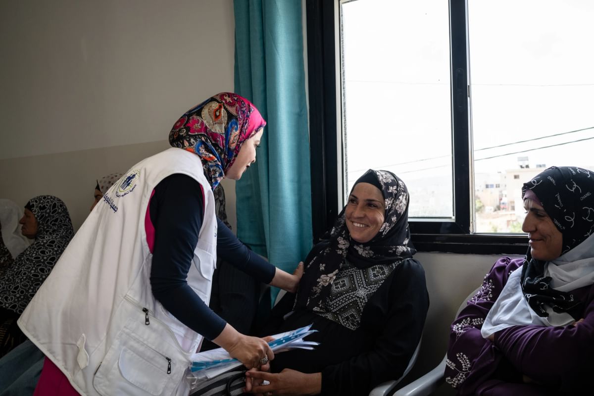 A medical professional speaks to two women in a mobile clinic, they are all laughing together