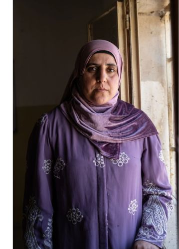 Kifah standing by a window wearing a purple dress and headscard