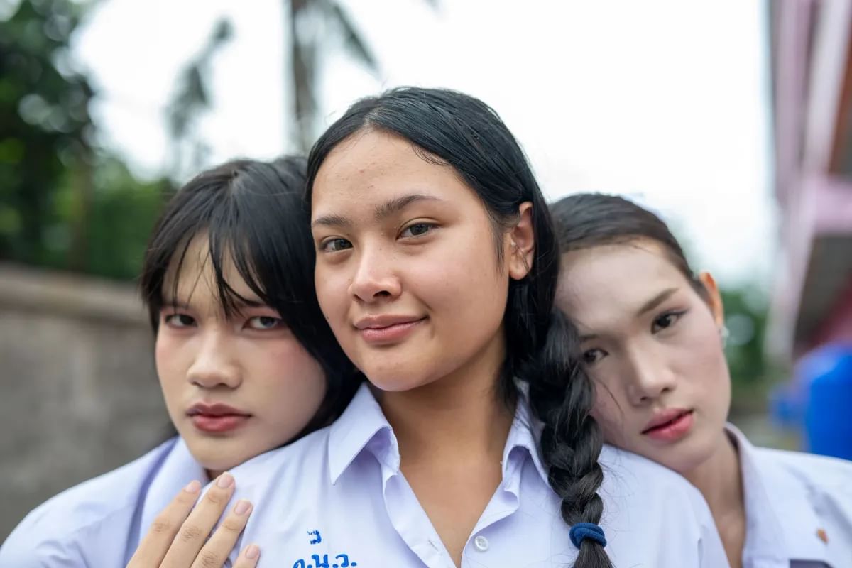 Three students from stand close together with their heads resting on each other looking directly at the camera 