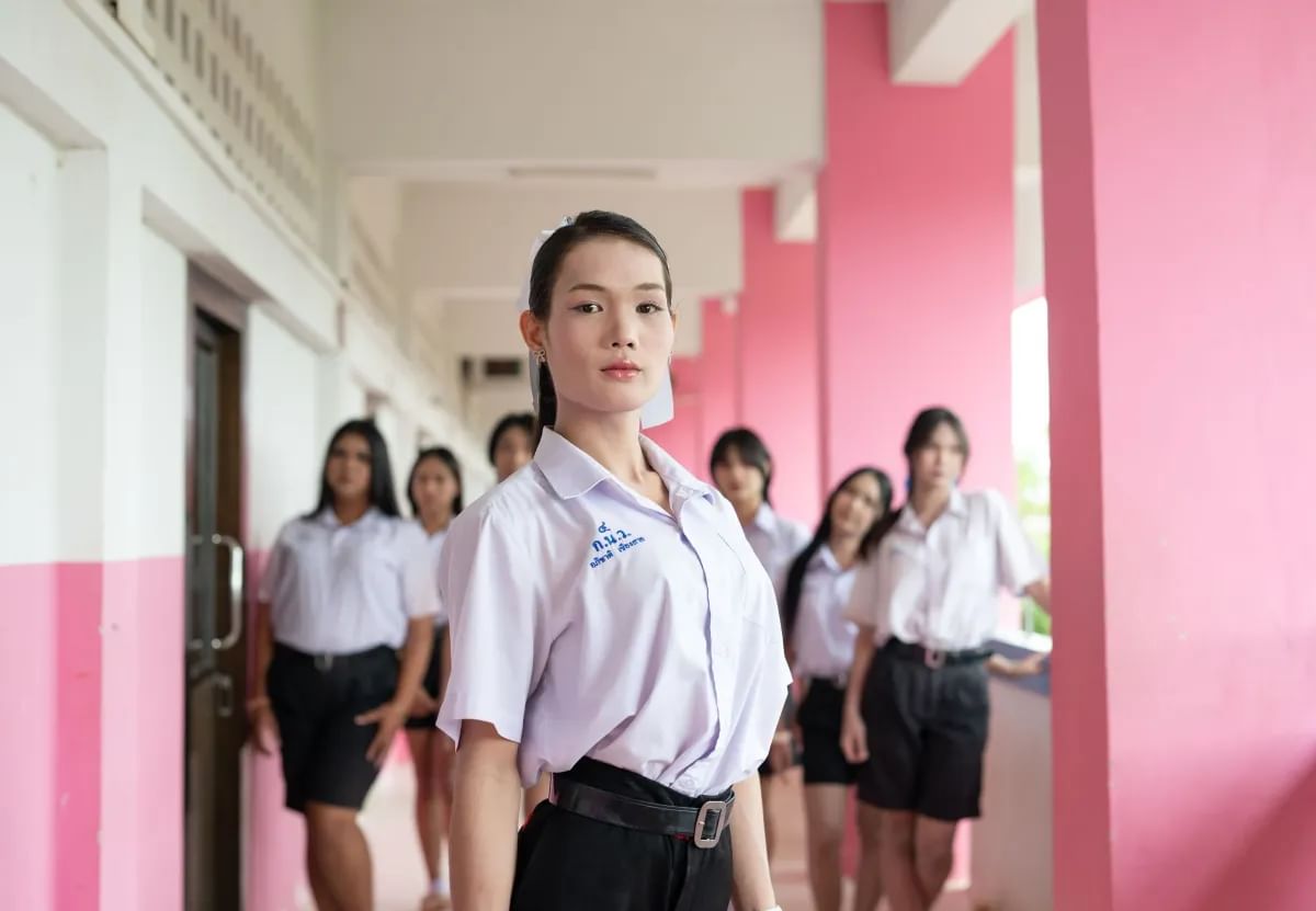 Seven students stand in an outside corridor looking at the camera. One student is close up to the camera with the others gathered around in the background.
