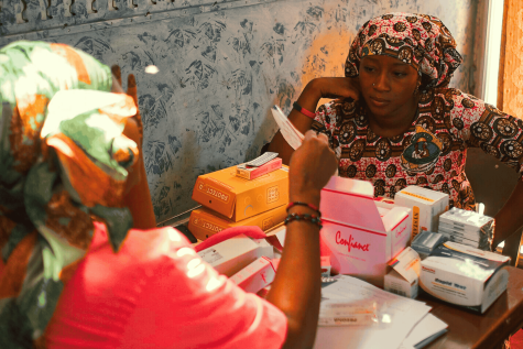 Two women sit at a table with boxes of contraceptives