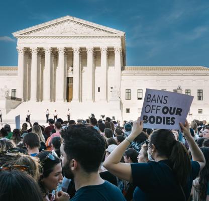 The US Supreme Court building with many protestors outside. One visible sign reads "Ban off our bodies"