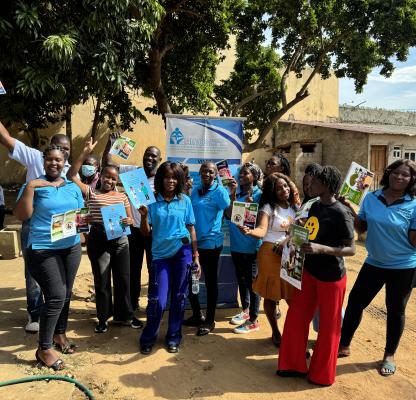 A group of peer educators gather in blue t-shirts waving leaflets and stood in front of a banner