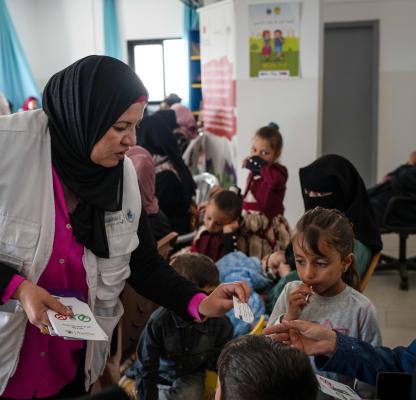 A healthcare hands out leaflets to mothers in a mobile clinic.