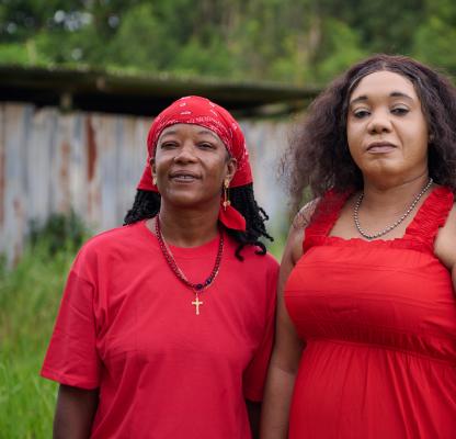 Two community workers in Suriname face the face camera, both dressed in red.
