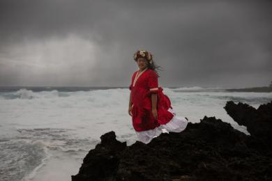 A person dressed in red stands in front of a stormy sea