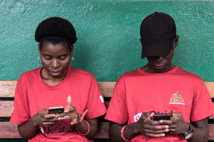 two young people sitting on a bench using their phones
