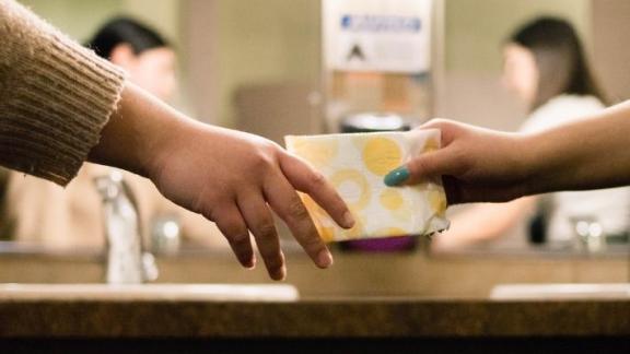 One hand passes a sanitary pad to another