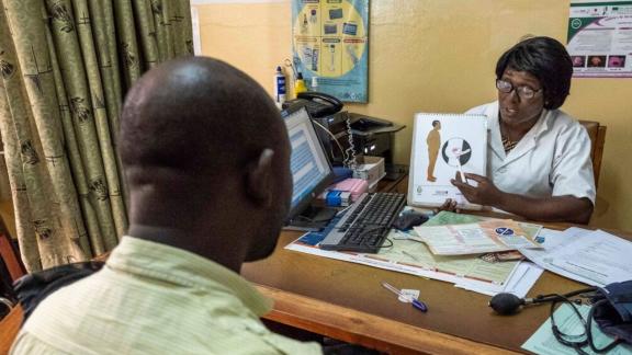 A healthcare worker demonstrates to a patient how a vasectomy works on a poster 