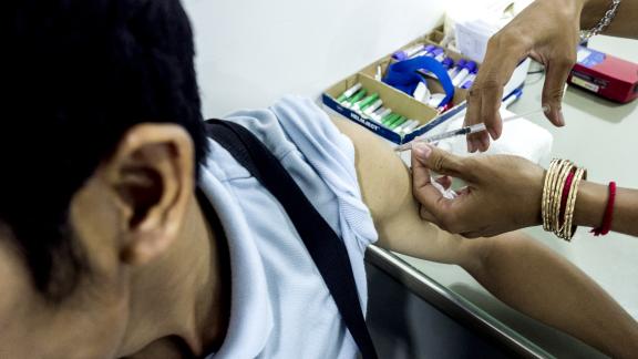 A man, who you cannot see his face is receiving a vaccination by a healthcare professional wearing medical gloves.