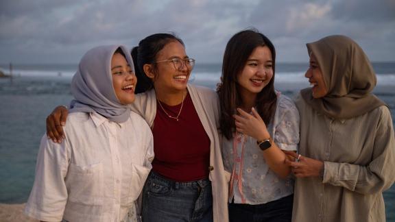 Three women stand together smiling with their arms around each other in Indonesia. 