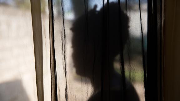 A women stands with her back to the camera, there is a black see through cloth between her and the camera. 