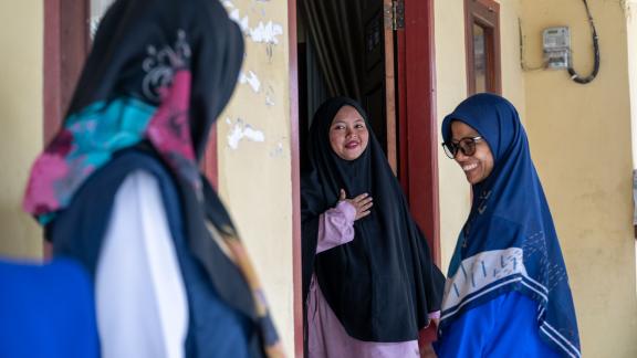 Three women stand together, one leaning out of an open doorway, and one with their back to the camera in Indonesia. 