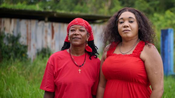 Two community workers in Suriname face the face camera, both dressed in red.
