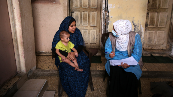 A health care professional speaks with a mother holding a baby. 