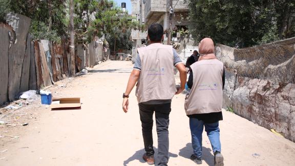 Two people walking away from the camera along a street of bombed buildings